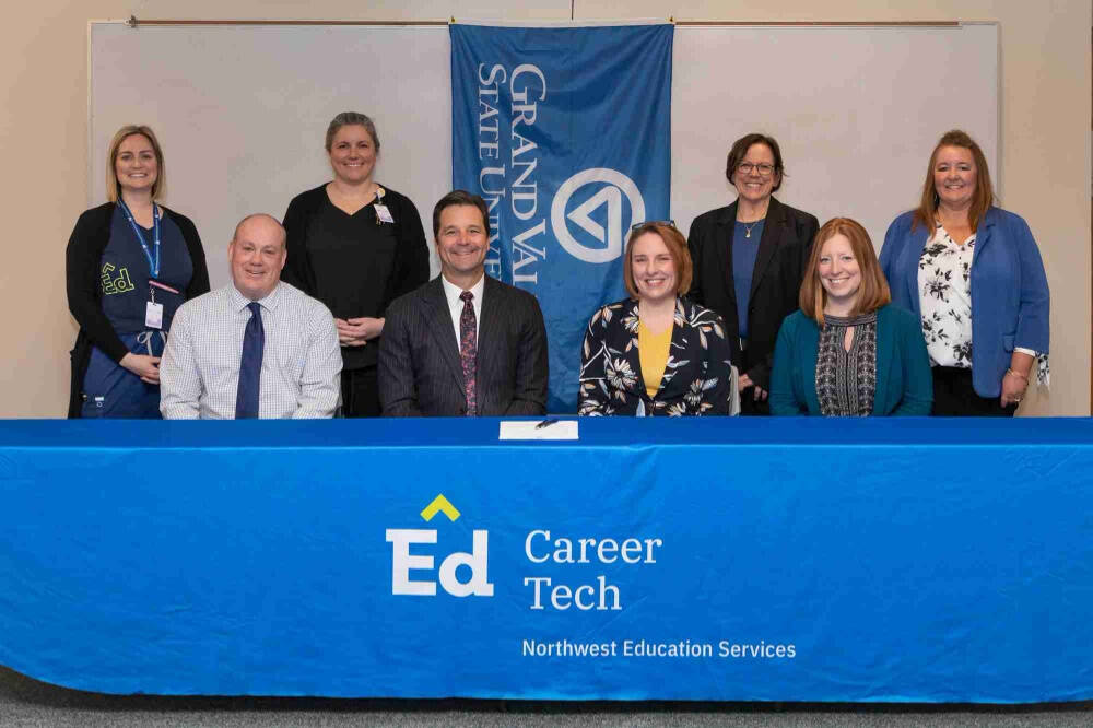 A group of eight people pose in front of a blue banner and tablecloth with university and career tech branding.
